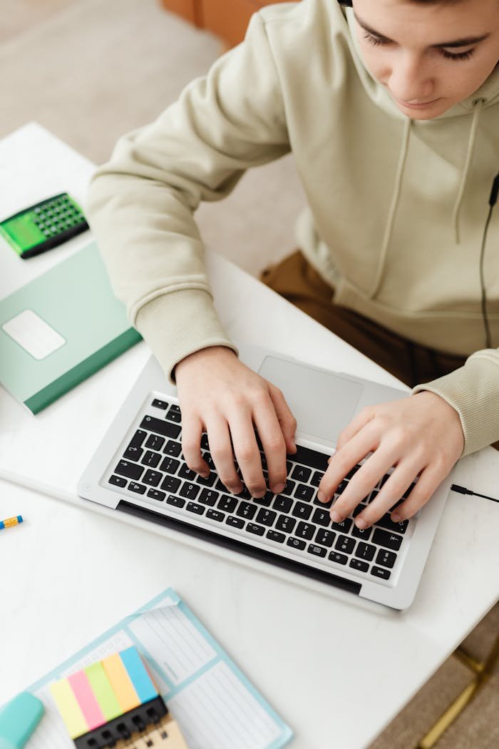 Crafting Captivating Headlines: Your awesome post title goes here Teenager in hoodie using a laptop for online education with study materials around.